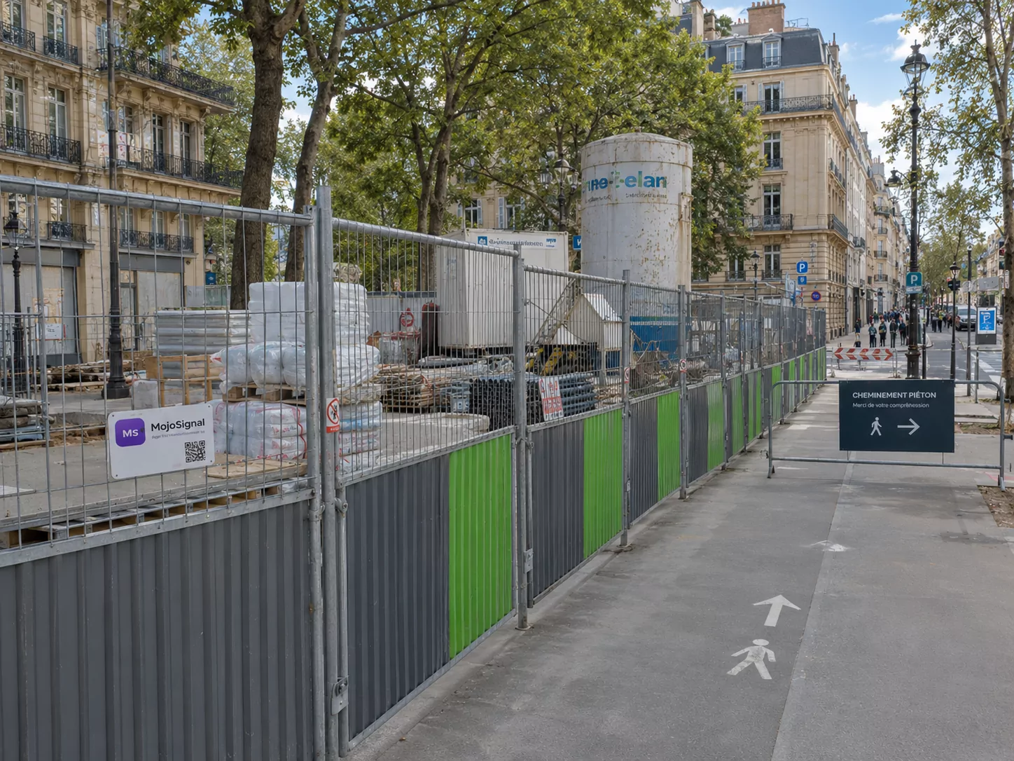 Chantier longue durée en ville avec clôtures de protection, panneau Mojo Signal et cheminement piéton sécurisé le long de l’emprise.