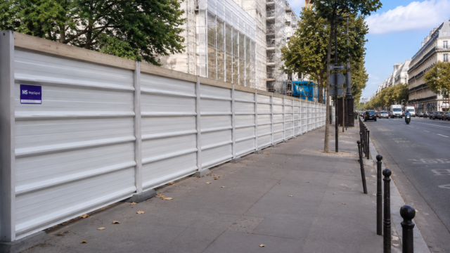 Long bardage blanc protégeant un chantier le long d’un boulevard urbain